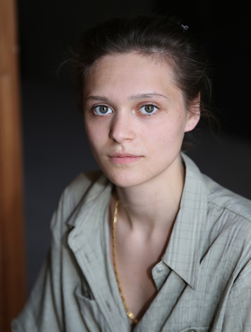 Antonia Siems Porträt einer jungen Frau mit dunklen zusammengebundenen Haaren, einem grauen Hemd und einer goldschimmernden Kette