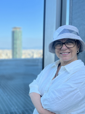 Sandra Vásquez de la Horra standing on a rooftop terrace, the city behind her. She's leaning against the wall, her arms crossed, smiling into the camera.